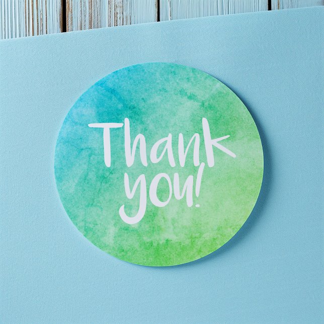 Adesivo de agradeço em aquarela verde brilhante (Round thank-you sticker with a blue and green watercolor gradient and handwritten-style white text)