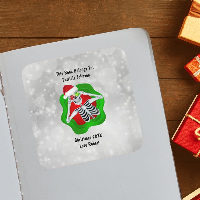 Adesivo Quadrado Esqueleto de Natal Ornamentos Vermelhos Brilhantes (Cute Skeleton holding ornaments for eyes Santa Hat in green Red splatter on white book plate sticker)