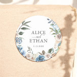 Adesivo Redondo Casamento Rustic Boho Dusty Blue Flowers<br><div class="desc">Introduzindo o nosso Sticker de Casamento Personalizado, uma mistura harmoniosa de prazer rústico e elegância contemporânea. Este adesivo maravilhosamente trabalhado apresenta uma charmosa camada de aquarela, mostrando um arranjo delicado de flores azuis e neutras. No coração deste abraço floral, seus nomes estão elegantemente inscritos em uma fonte serif clássica, conectada...</div>