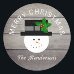 Adesivo Redondo Farmhouse Christmas Snowman Family Name<br><div class="desc">Farmhouse Christmas Snowman Family Name Classic Round Stickers são projetados com fundo de madeira de celeiro sujo. Um bonitinho bonitinho está no centro e "Feliz Natal" está curvado sobre sua cabeça. Personalizado com o sobrenome da família em letras brancas de escrita caligráfica na área inferior dos autocolantes. CLIQUE EM PERSONALIZAR...</div>