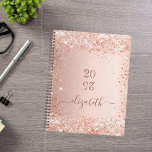 Agenda Nome do monograma da poeira dourada do rosa Blush<br><div class="desc">Um fundo rosa dourado com poeira brilhante elegante. Personalize e adicione um ano (invertido) e adicione um nome. O nome é escrito em ouro rosa escuro com um grande roteiro de estilo, escrito à mão, com baloiços. Perfeito para a escola, o trabalho ou a organização da sua vida pessoal/familiar. Para...</div>