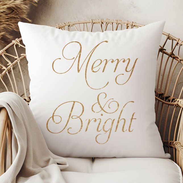 Almofada Feliz e Brilho - Travesseiro de Natal Dourado e br (Merry & Bright - Gold and White Christmas Pillow on a boho rattan armchair.)