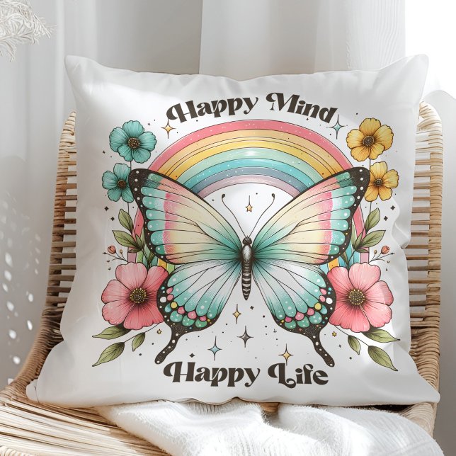 Almofada "Mente Feliz Vida Feliz" Pastel Borboleta Rainbow ("Happy Mind Happy Life" Pastel Butterfly Rainbow Throw Pillow in a sunny rattan armchair.)