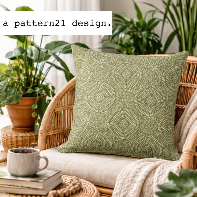 Almofada padrão verde boêmio (Olive geometric accent pillow styled in a bright plant-filled living space.)