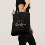 Bolsa Tote Monograma com brilho dourado preto elegante<br><div class="desc">Um fundo preto elegante. Personalize e adicione seu nome,  siglas monográficas. Seu monograma como padrão de fundo. O nome é escrito com um script de estilo manuscrito. Letras brancas e ouros.</div>