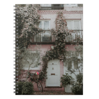 CADERNO ESPIRAL CASA PINTA E BRANCA COBERTA POR PLANTAS A