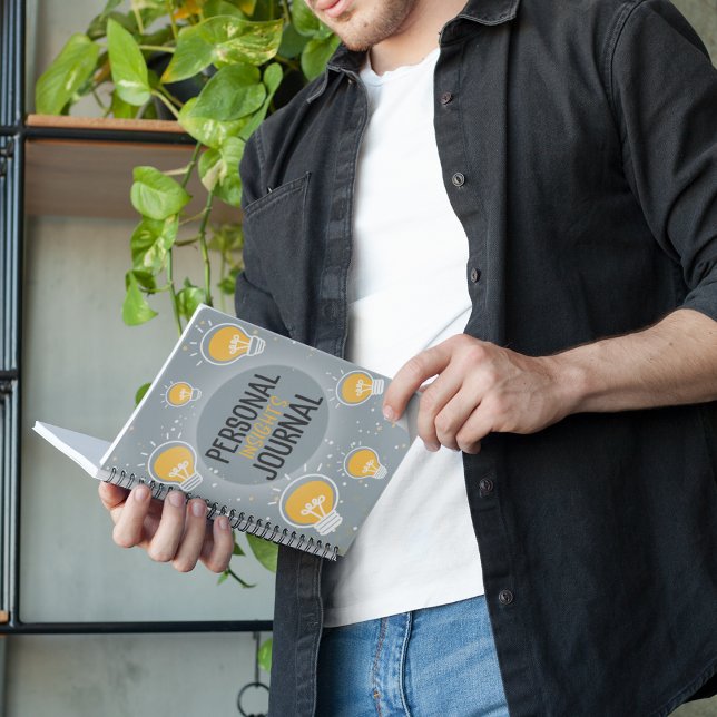 Caderno Espiral Notebook Diário Personal Insights Lightbulb (A man looking at his notebook which is entitled Personal Insights Journal, covered in lightbulbs)