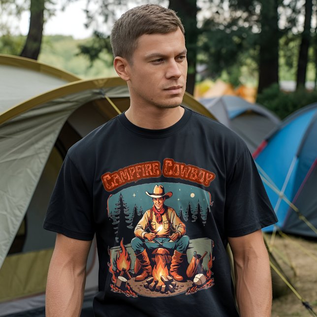 Camisa Gráfica Western Cowboy Retro em Torno da Fo (A man wearing a black t-shirt with a "Campfire Cowboy" graphic design, standing in front of a camp)