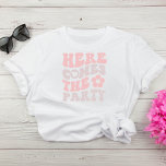 Camiseta Festa de solteira de Script Retroativo de Corte<br><div class="desc">Camiseta de festa de solteira bonita com "Here Vem The Party" em uma fonte retrorada cor-de-rosa-laranja e esticada e uma ilustração de uma flor de estilo 70. Uma jaqueta de "Aqui Vem A Noiva" está disponível para a noiva.</div>
