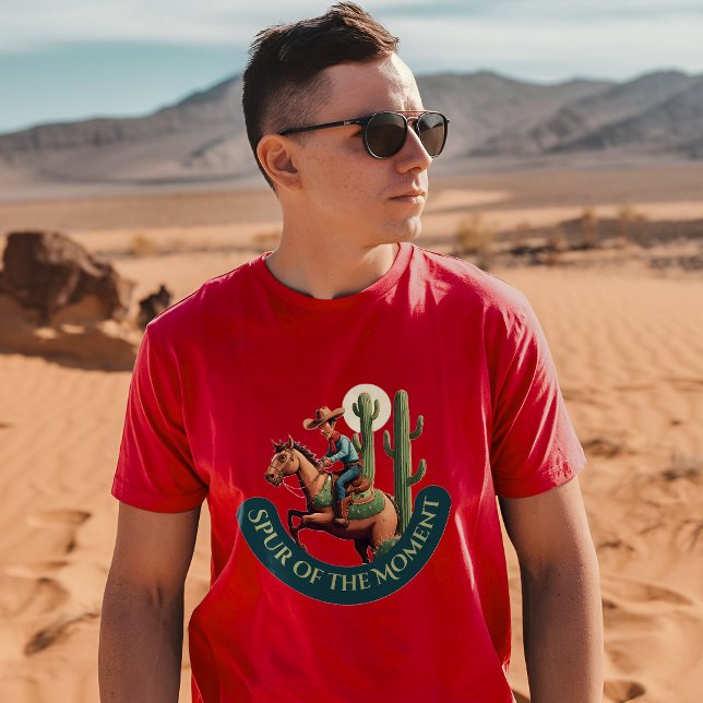 Camiseta Impulso do Momento Gráfico do Cowboy (A man wearing a cardinal t-shirt with a cowboy and cactus design stands in a desert landscape)