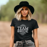 Camiseta Presente de Festa de casamento de Noiva da Equipe<br><div class="desc">O Design de Tipografia Elegante Moderna e Moça Tímica Gira em Grito Lê "Noiva de Equipe" com Rico Scroll Frame Border. Presente perfeito para noiva, damas de noiva e festa de casamento para vestir enquanto se prepara no dia do seu casamento! Clique no botão "Personalizar" para personalizar a frente com...</div>