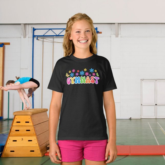 Camiseta T-shirt do ginasta Retro | T-shirt temática "ginás (A young girl wearing gymnast black t-shirt with flower power style retro design. Gymnasium behind.)