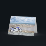 Cartão 70th birthday card with a motor bike<br><div class="desc">A blue motor cycle standing on a beach with fluffy clouds in the sky. Happy Birthday written in rock reflected in the water lying on the sand.</div>