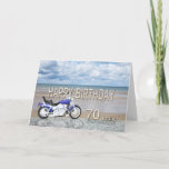 Cartão 70th birthday card with a motor bike<br><div class="desc">A blue motor cycle standing on a beach with fluffy clouds in the sky. Happy Birthday written in rock reflected in the water lying on the sand.</div>