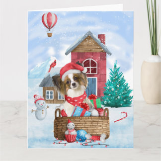 Cartão Cão Papillon na casa de Natal na neve