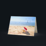 Cartão Christmas starfish on the seashore with seagulls<br><div class="desc">starfish wearing red and white furry Santa hat on the beach with seagulls and blue water background</div>