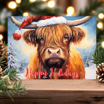 Cartão De Festividades Highland Cow Santa Hat - Festa de Natal<br><div class="desc">Celebrar a época de férias com este adorável cartão de Natal com uma encantadora vaca Highland vestindo um chapéu de Papai Noel. A cena festiva inclui árvores cobertas de neve e uma saudação alegre de "Feliz Feriados" em vermelho. Perfeito por adicionar um toque de reluz e calor aos seus cartões...</div>