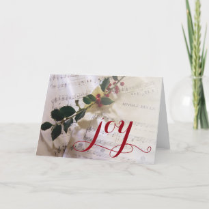 Cartão De Festividades Holly branch on top of sheet music for Christmas