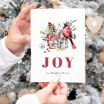 Cartão postal de Natal para aves cardinhas de cor<br><div class="desc">Este aconchegante cartão de Natal apresenta uma ilustração aquática de um cardeal vermelho gravado sobre uma coleção de presentes de Natal embrulhados por presente e cercado por verde sagrado e embleto e flocos de neve azuis estilizados. A palavra "JOY" aparece em letras grandes e sujas vermelhas que se coordenam com...</div>