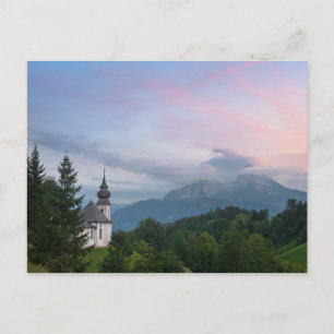 Cartão Postal Igreja com montanhas alpinas no pôr do sol