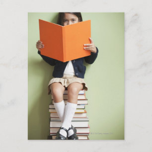 Cartão Postal Rapariga de raça mista sentada em pilhas de livros