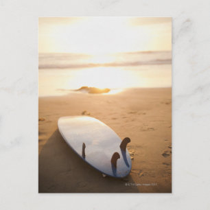 Cartão Postal Surfboard na praia no pôr do sol