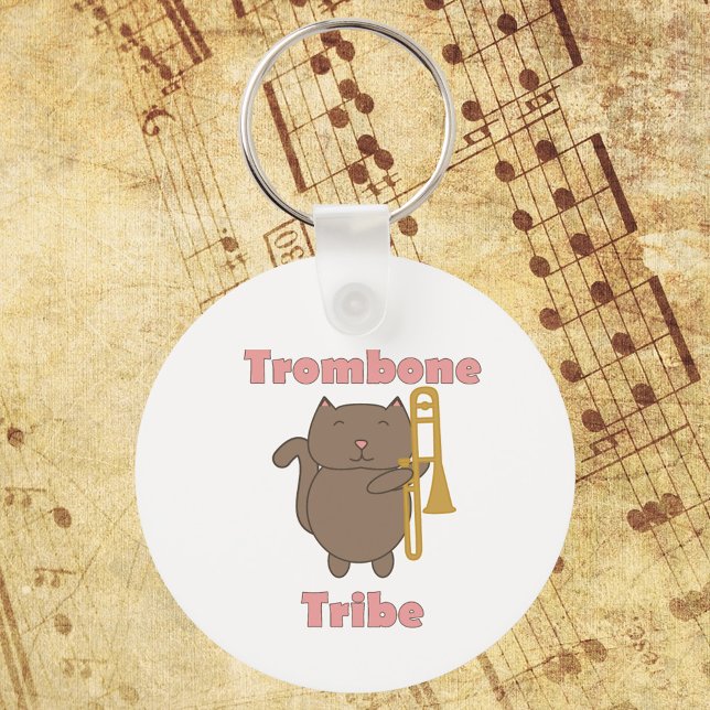 Chaveiro Tribo do Trombone Gatinho Fofo Letras Rosa (A keychain with a brown cat holding a trombone and the words trombone tribe in pink.)