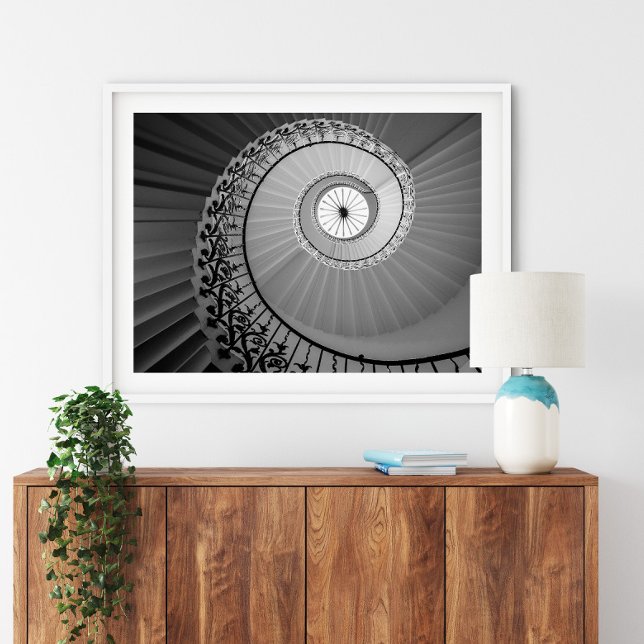 Escadaria Espiral com Poster de Flores (Spiral Staircase with Flowers Poster in a white frame above a small furniture.)