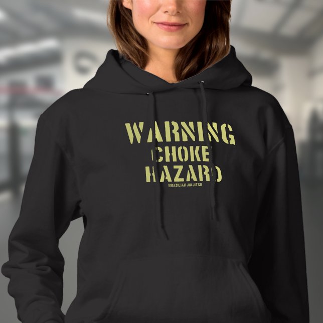 Moletom BJJ Aviso Choke Hazard Brasileiro Jiu Jitsu (Choke hazard woman's black hoodie worn by a female model in a gym.)
