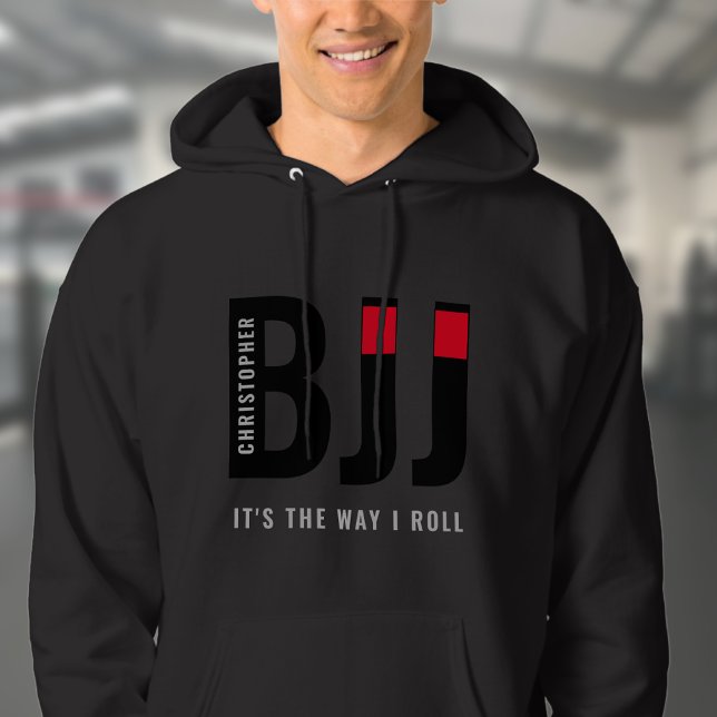 Moletom BJJ brasileiro Jiu Jitsu adiciona nome Black Belt (Unisex black BJJ hoodie worn by male model in a gym.)