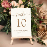 Numeração De Mesa Recepção de casamento de Creme de Script Dourado C<br><div class="desc">Sinal de número da tabela de recepção de casamento de creme leve com "mesa" em um roteiro elegante de caligrafia dourada com baloiços, o número da tabela na tipografia clássica da serifpografia dourada, seus primeiros nomes unidos por um coração e sua data de recepção. Crie cada número de tabela e...</div>