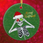 Ornamento De Cerâmica Bobo Natal Skeleton Hat Ornaments Green<br><div class="desc">Este ornamento cerâmico pendurado tem um esqueleto de bobo segurando ornamentos vermelhos e verdes até seus olhos enquanto sorri e veste um chapéu vermelho de Papai Noel em um fundo verde com speck falsos de ouro. Feliz texto de Natal em ouro na frente. Personalize o texto no verso com o...</div>