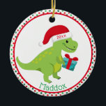 Ornamento De Cerâmica Dinossauro Verde com Santa Hat Personalizado<br><div class="desc">Dinossauro verde bonito está vestindo um chapéu vermelho de Papai Noel e carregando um presente azul. A borda é bolinhas vermelhas e verdes. Personalize com o nome dos seus filhos no fundo e no ano no chapéu dele. O lado inverso é o mesmo design.</div>