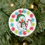 Ornamento De Cerâmica Feliz Snowman Snowflake - Netos da Frame<br><div class="desc">Este Enfeites de natal bonito mostra uma imagem de um bonitinho de neve vestido de vermelho e verde, e segurando uma bengala listrada. O boneco de neve é armado com flocos de neve dourados, vermelhos e azuis. A parte de trás do ornamento tem o mesmo quadro de floco de neve...</div>
