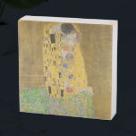 Os amantes beijando o abraço de Gustav Klimt<br><div class="desc">A luz do sol brilha do abraço do ouro que rodeia os amantes da obra-prima de Gustav Klimt, The Kiss. A cena é um paradoxo de intimidade e isolamento. O casal está sobre um precipício, um campo de flores coloridas em seus pés, mas elas estão indiferentes ao mundo ao seu...</div>