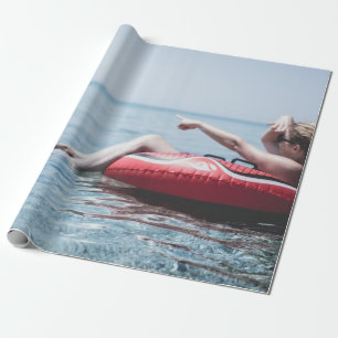 Papel De Presente Mulher em um flutuador inflável no oceano apontand