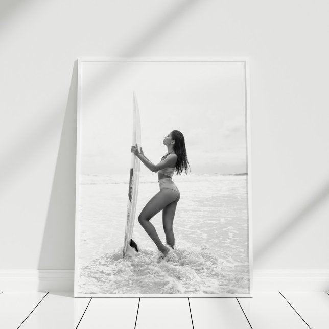 Poster Surfista Negra e Branca na Praia (Black and White Surfer Girl on the Beach Poster in white frame on wooden floor.)