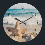 Relógio Grande Starfish em uma fotografia de Sandy Beach<br><div class="desc">Um relógio com uma foto cênica. Um grande peixe-estrela colocado em pé numa praia arenosa. Um belo mar azul com ondas de surf branco no fundo.</div>