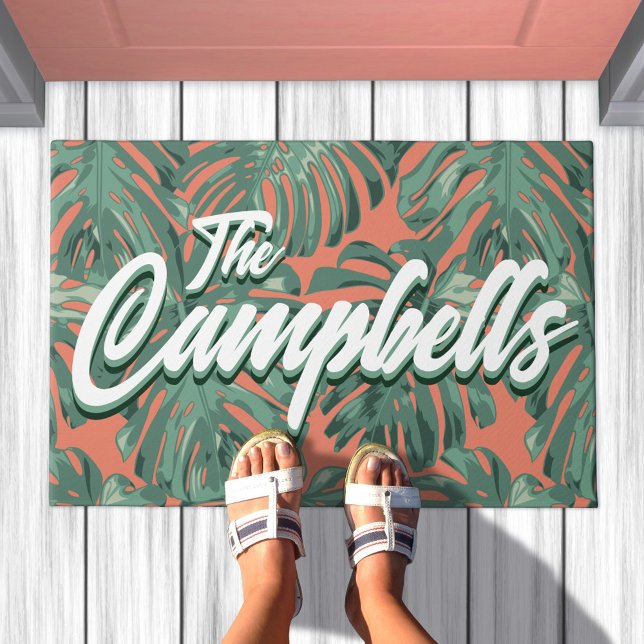 Tapete Porta de Nome Verde da Família Tropical (Doormat with green leaves on orange background. Text overlay says your family name)