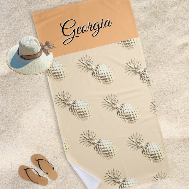 Toalha De Praia Pêssego Personalizado de Nome Pineanases Elegante (A beach towel with faux gold pineapples print, personalized with a name in elegant script typography)